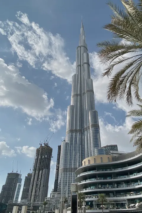 The Burj Khalifa in Dubai with palm trees, under a blue sky with white clouds.