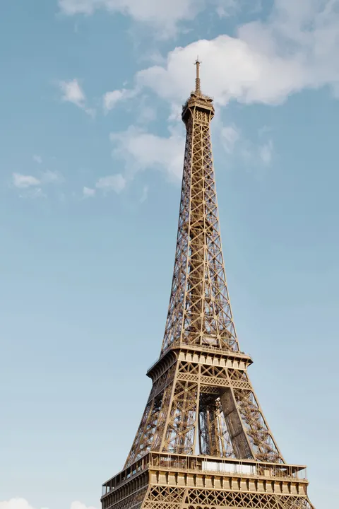 The Eiffel Tower in Paris against a blue sky with white clouds.